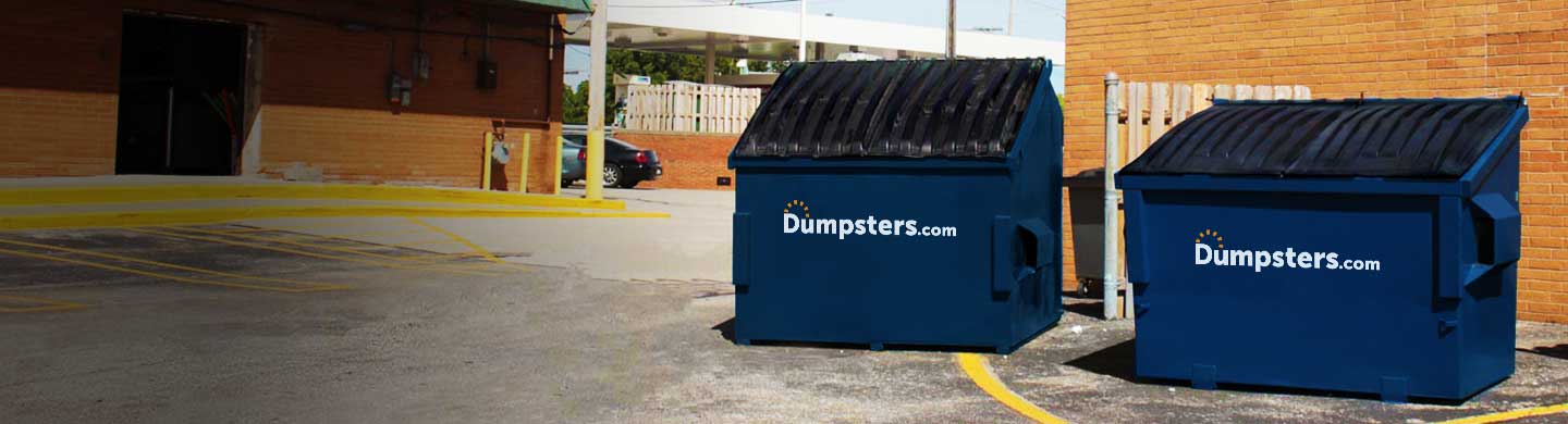 two front load dumpsters next to each other beside a brick wall