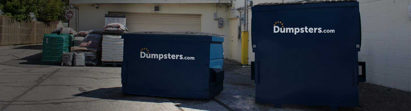 two permanent dumpsters of various sizes in a commercial parking lot