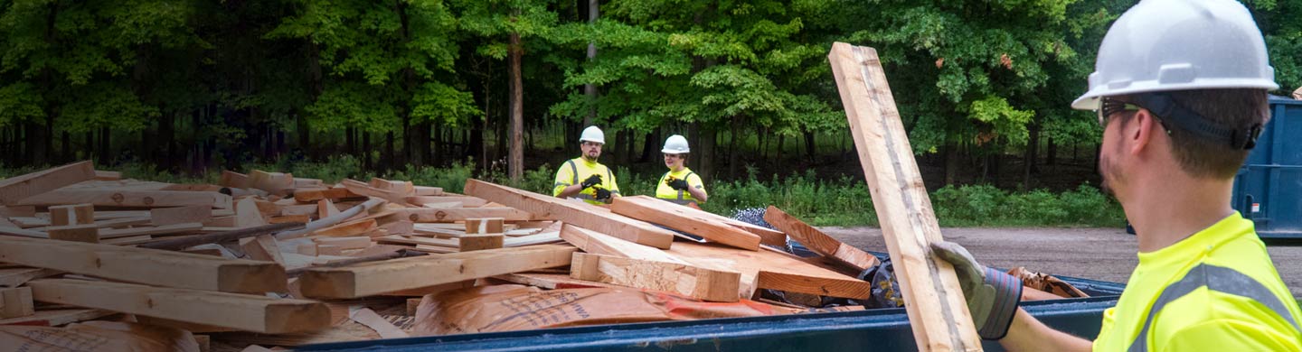 Builder with board and two workers in background.