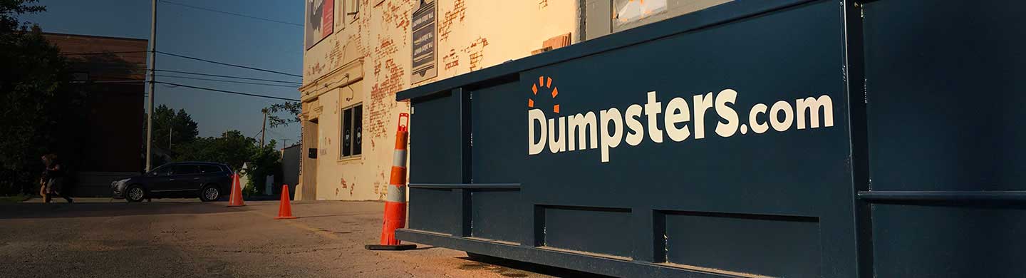 dumpster placed on a street surrounded by orange cones