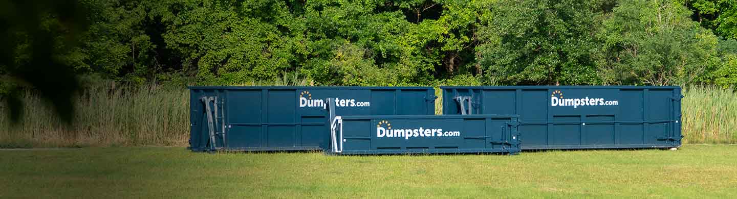 three dumpsters of various sizes in a field