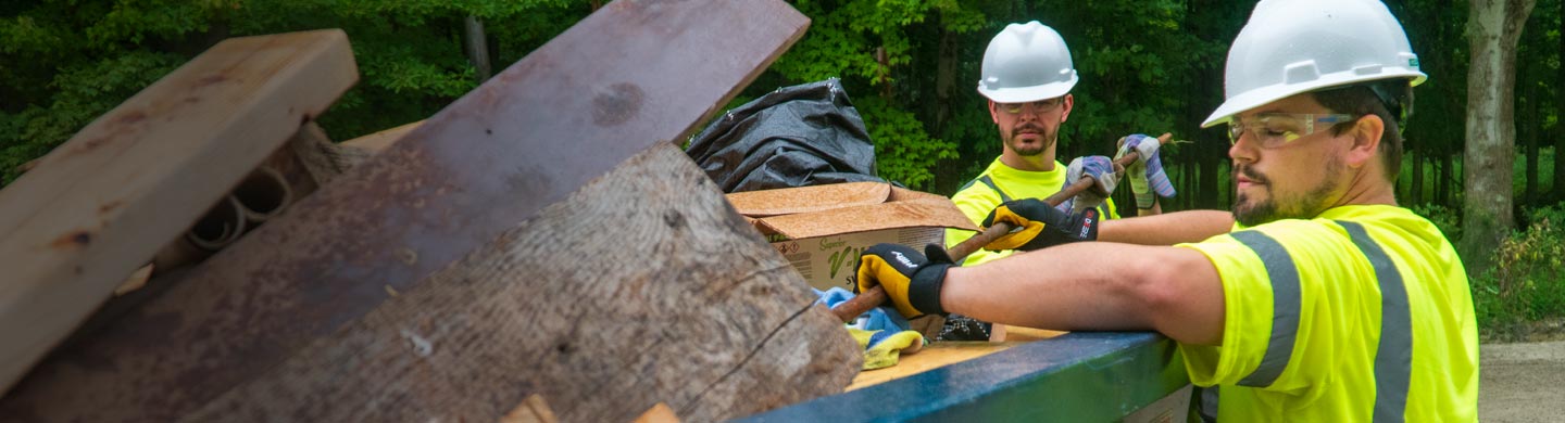 construction workers placing debris in a roll off dumpster