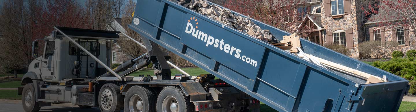 a roll off dumpster filled with heavy debris being loaded onto a truck