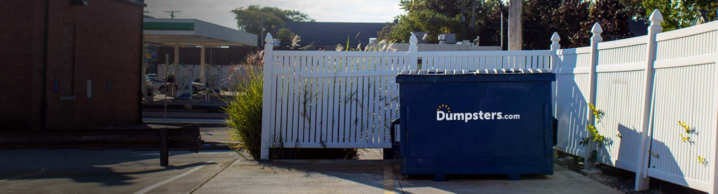 commercial dumpster in front of white fence enclosure