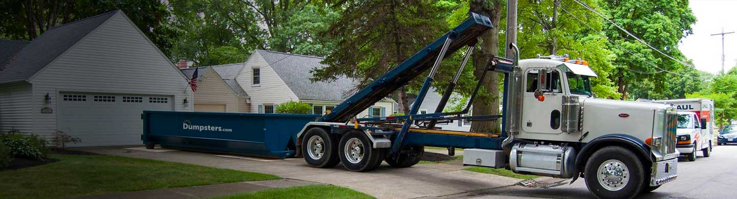 truck unloading roll off dumpster in driveway