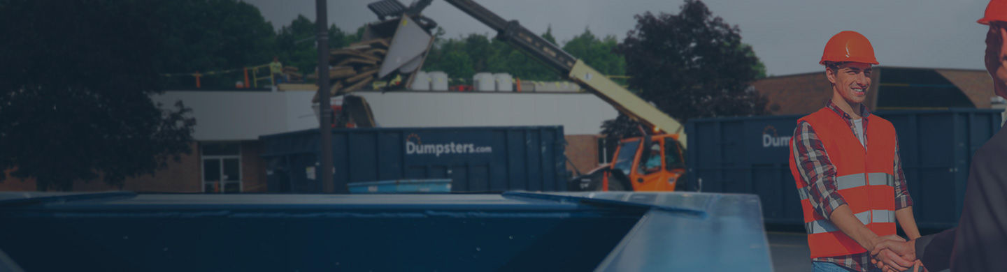 Construction project manager on a jobsite with dumpsters.com bins in the background