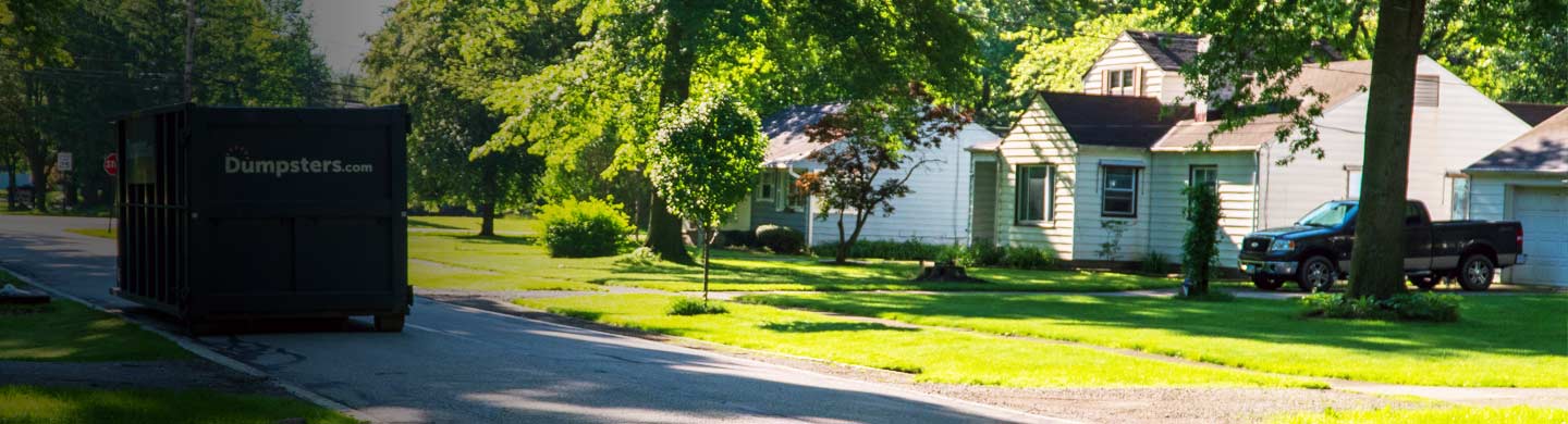 roll off dumpster on a driveway beside a green yard