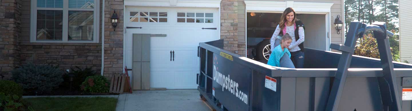 Mother and Daughter Loading Junk into Blue Residential Dumpster in Front of Nice House