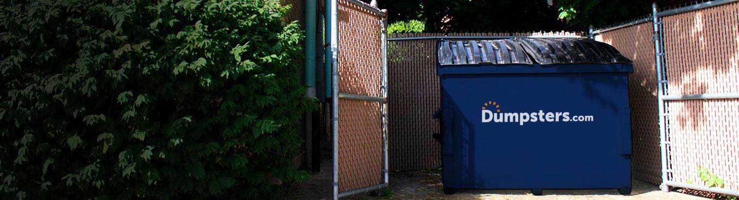 A Dumpsters.com commercial dumpster placed within an enclosure on a business property.