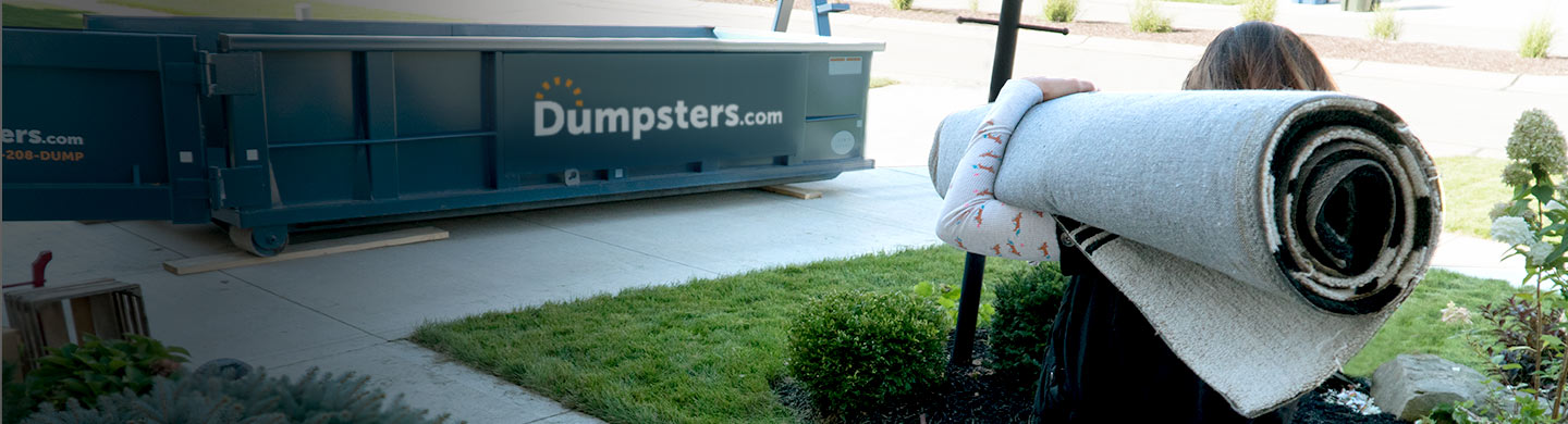 woman carrying a rolled up carpet to a dumpsters.com dumpster