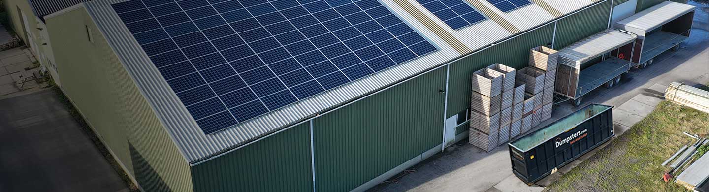 A Dumpsters.com dumpster sitting next to a large facility covered in solar panels.