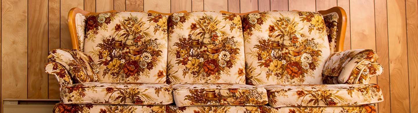 A floral patterned couch with wood frame in front of a wood-panel covered wall.