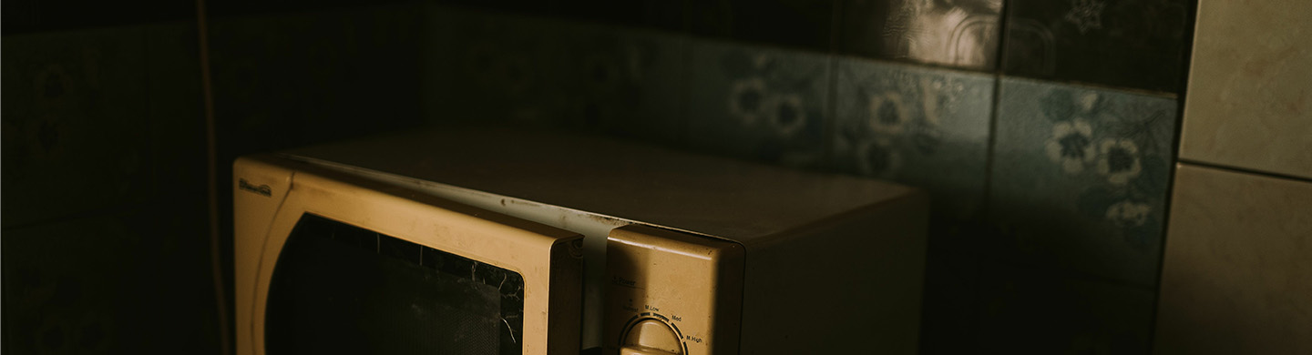 A close-up of an old microwave against a backsplash.