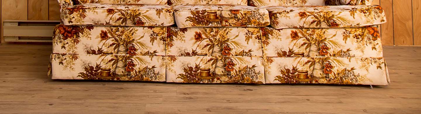 A floral patterned couch with wood frame in front of a wood-panel covered wall.