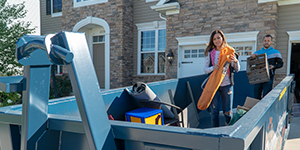 People loading debris into a roll off dumpster.