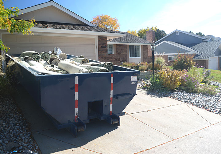 Roll Off Dumpster Filled with Carpet and Junk Sitting on Residential Driveway.