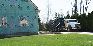 A dumpster truck picking up a dumpster at a new home build