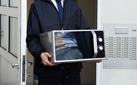 Man carrying used microwave out of his apartment.