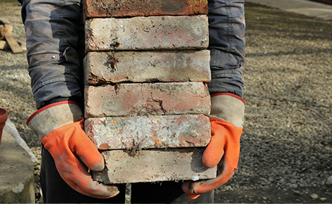 Junk removal worker with gloves carrying a stack of bricks.