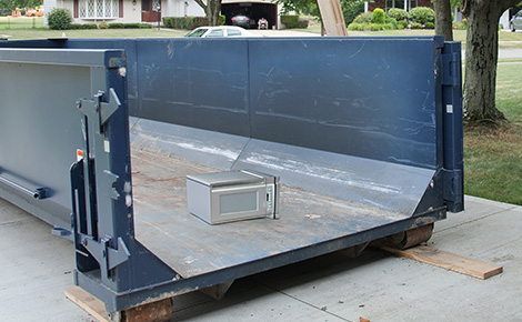 Microwave sitting at the bottom of an empty dumpster.