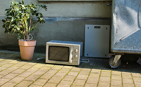 Microwave sitting curbside next to trash receptacle.