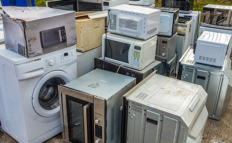 Microwaves stacked in pile of appliances at recycling center.