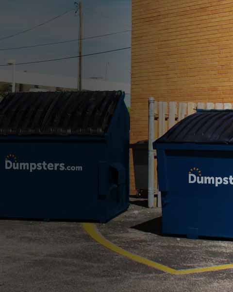 two front load dumpsters next to each other beside a brick wall