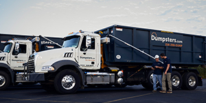 Drivers standing next to a line of dumpsters.com trucks