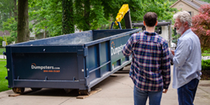 two customers watching a dumpster be delivered at their home