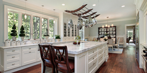 renovated kitchen with chrome pots hanging above a marble topped island and antique wood floors