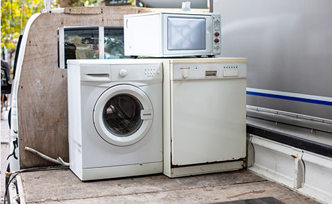 Old microwave stacked on washer and dryer on back of junk removal vehicle.