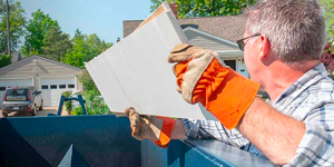man throwing a white board in a dumpster