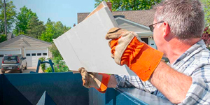 contractor throwing a board in a roll off dumpster