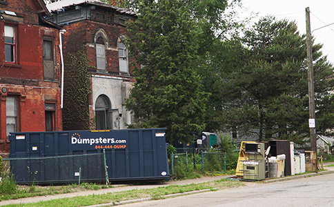 Roll Off Dumpster in Front of Historic Brick Building With Trash on Curb