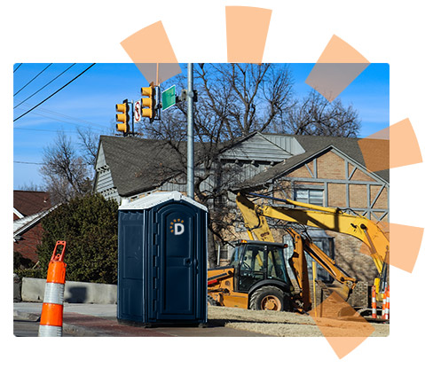 Dumpsters.com portable toilet on a construction site sitting next to a backhoe with an orange traffic cone in the foreground.