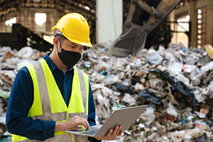 A plant worker at a recycling facility enters data into a laptop on-site.