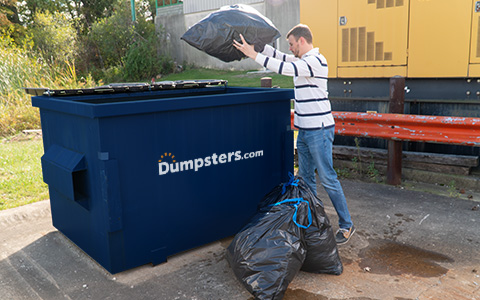 Man Throwing Trash Bags Into Front Load Dumpster.