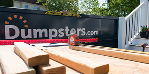 Wood blocks and measuring tape in front of a dumpsters.com dumpster. 