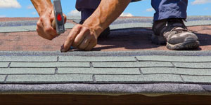 A Man Nailing Asphalt Three-tab Shingles to a Roof