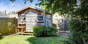 A wooden shed in a fenced-in yard.