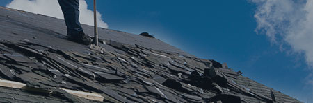 foot of roofer scraping shingles from roof with blue sky in background