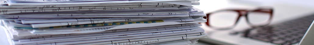 Stack of Papers Next to a Pair of Glasses and a Laptop.