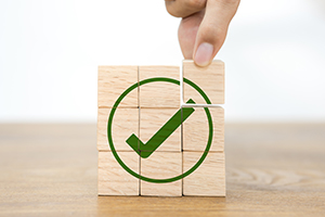 A stack of wooden building blocks that make a green checkmark inside a green circle on the front once assembled.