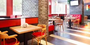 A well-lit restaurant with wooden tables, wooden floors and red color schemes with grey, brick accent walls.