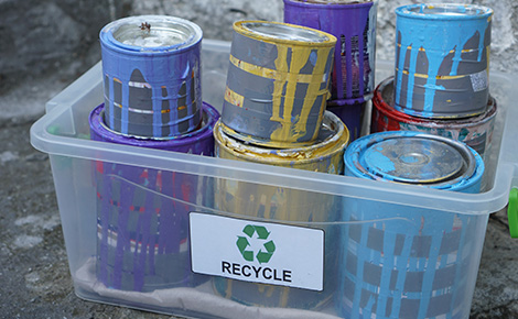 Cans of used paint stacked inside of recycling bin. 