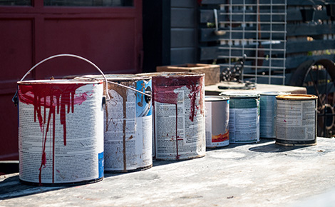Cans of used paint sitting outside on concrete.