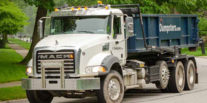 A Dumpsters.com roll off dumpster truck driving down the street