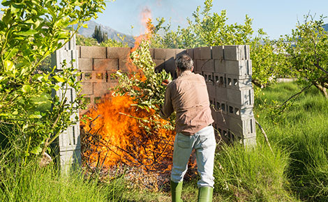 Man burning yard waste in an enclosed cinderblock area.